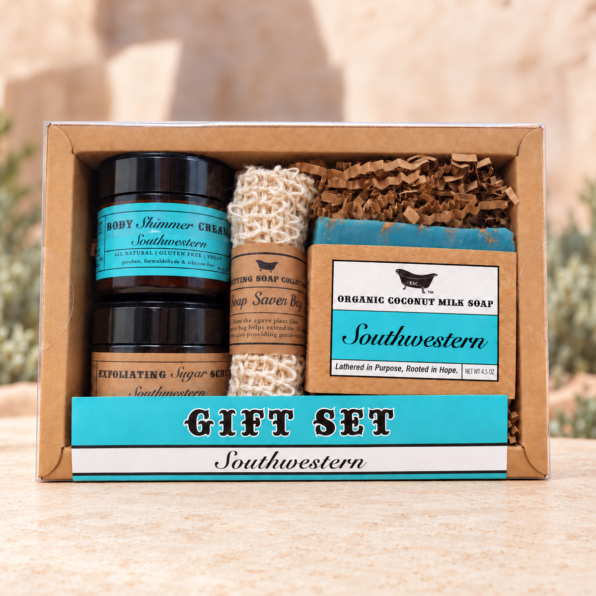 A boxed gift set containing two black jars of Southern-themed body cream, a wrapped soap bar, and shredded brown paper filler inside a kraft gift box with turquoise and white labels.